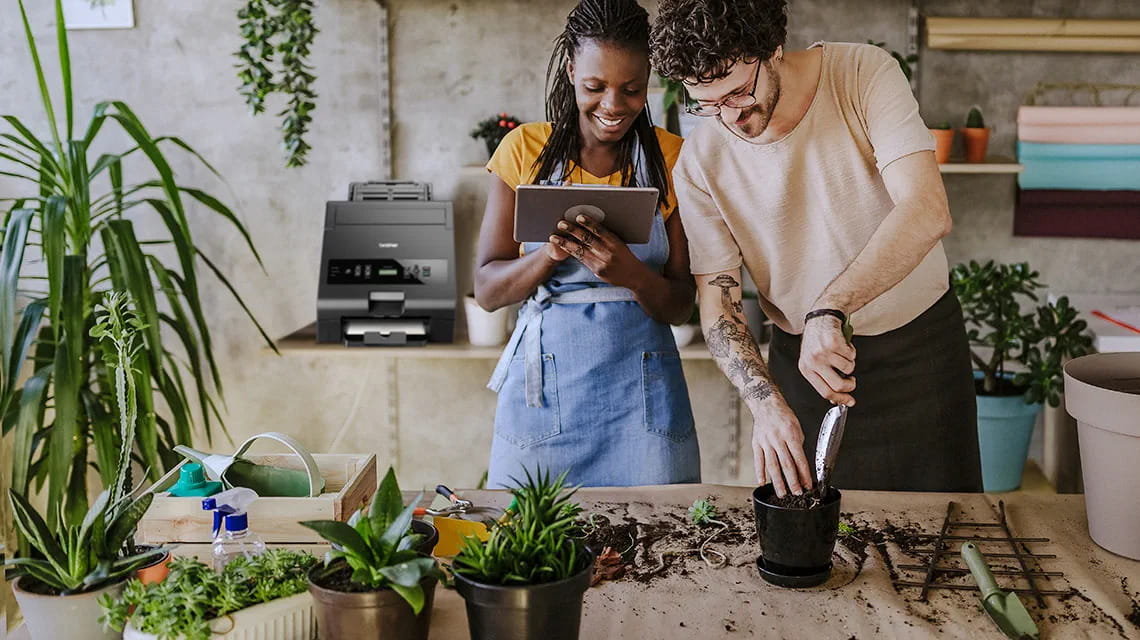 Woman and man in flower shop potting plants, HAK hot foil printer in the background